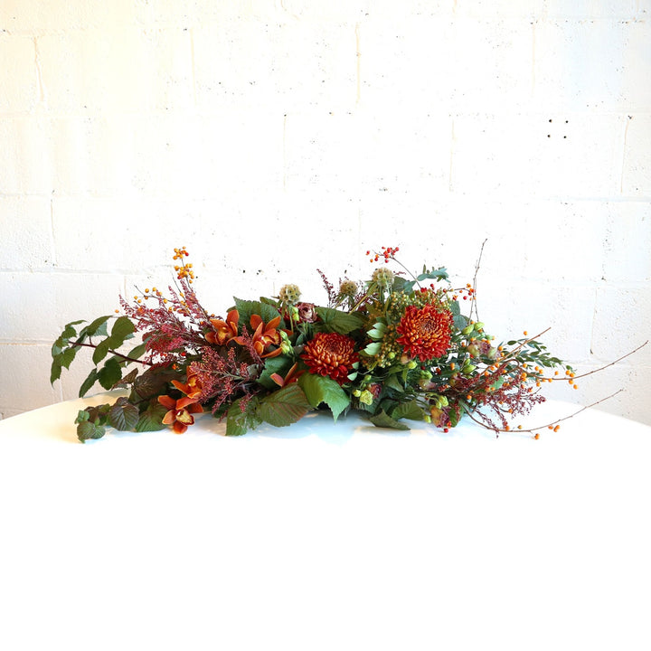 Autumn Centerpiece | A long and low arrangement perfect for your holiday table! Red, orange, and greens with berries and a variety of greenery. Photo taken against a white background.