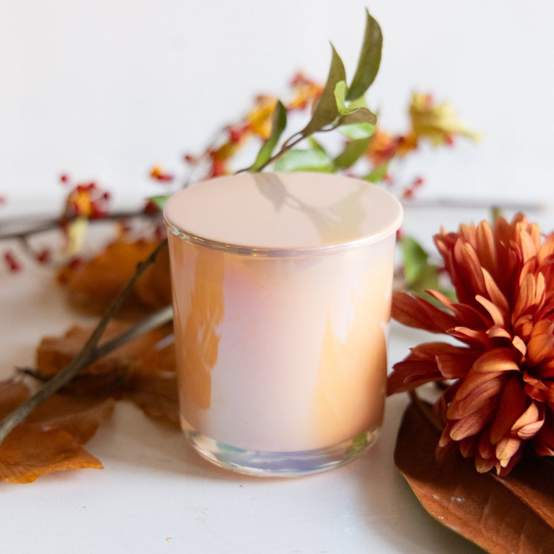 Candle in a glass holder with autumn leaves and flowers on a white surface