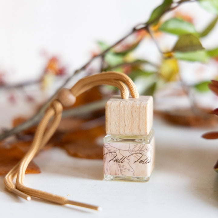 Small glass bottle with wooden cap on a white surface with blurred autumn leaves in the background