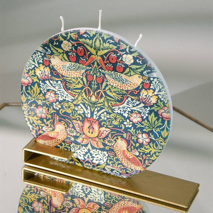Decorative candle with floral and bird pattern on a stand against a neutral background
