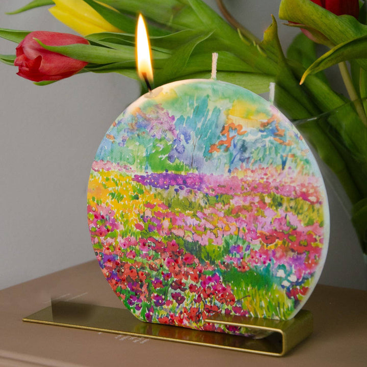 Decorative candle with floral design next to a bouquet of tulips