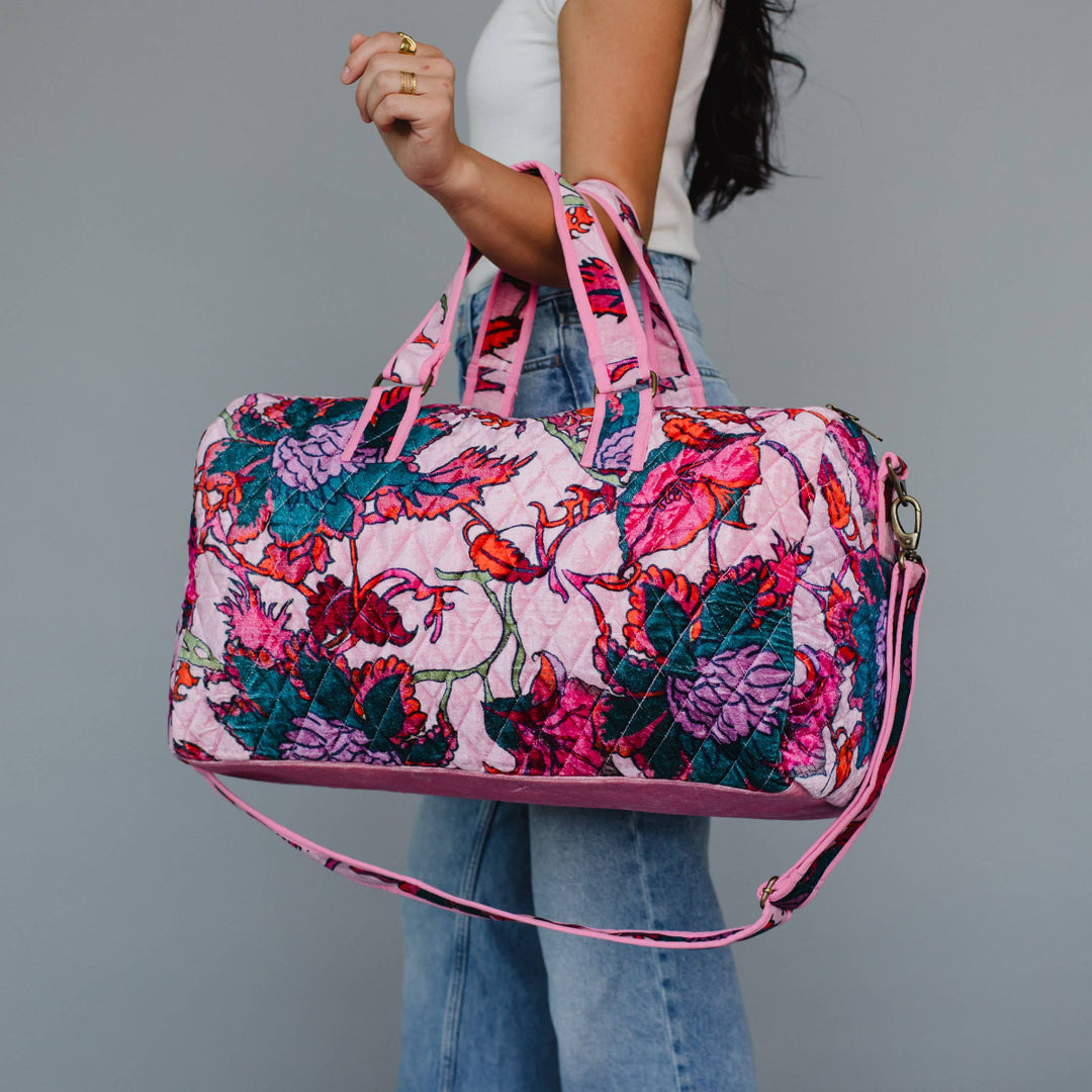 Person holding a floral patterned handbag with pink straps against a gray background
