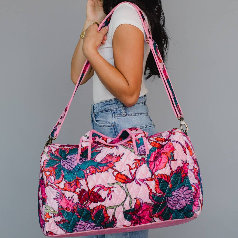 Person holding a pink floral duffel bag against a gray background