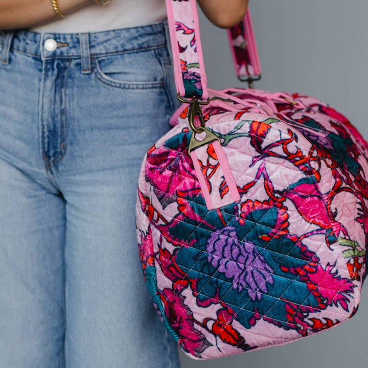 Person holding a colorful quilted bag with a pink strap against a gray background