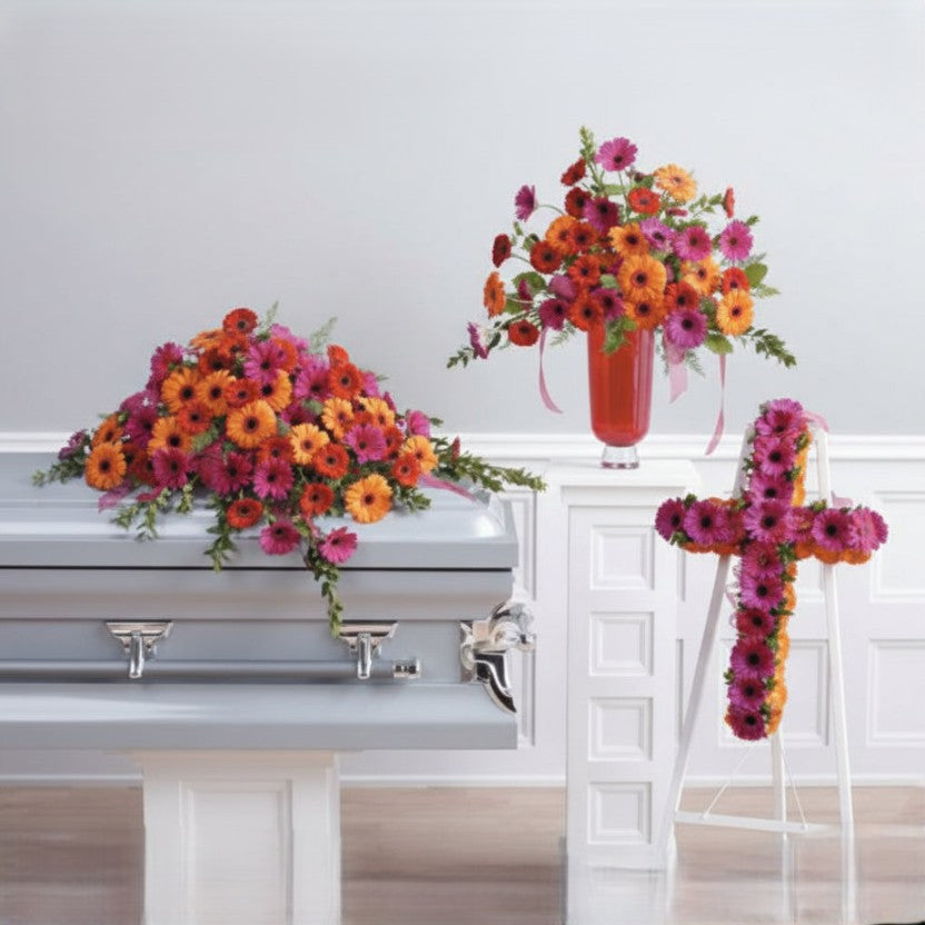 Floral arrangements and a cross made of flowers on a casket against a white wall.