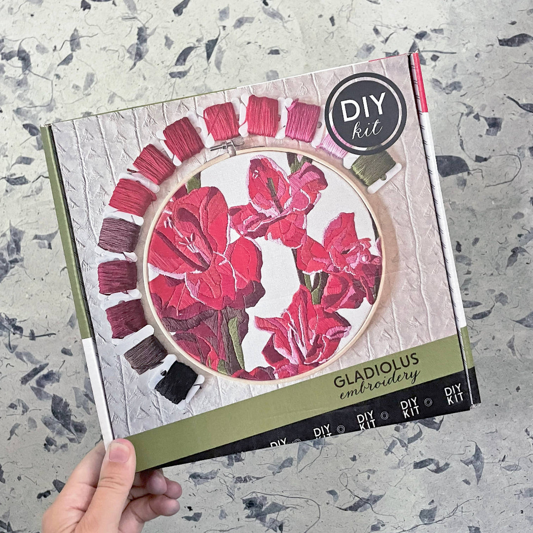 DIY gladiolus embroidery kit packaging held by a hand on a textured surface