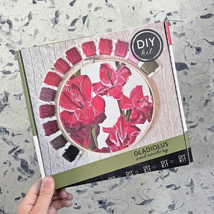 DIY gladiolus embroidery kit packaging held by a hand on a textured surface