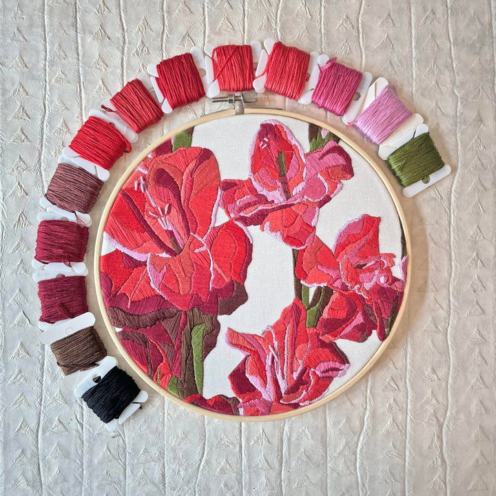 Embroidery hoop with red floral design and colorful thread spools on a textured beige background