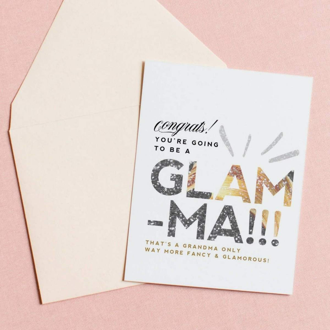 A white card with simple black, and sparkly text that reads "Congrats! You're going to be a Glam-ma. That's a grandma on way more fancy and glamorous!". Comes with a cream envelope.