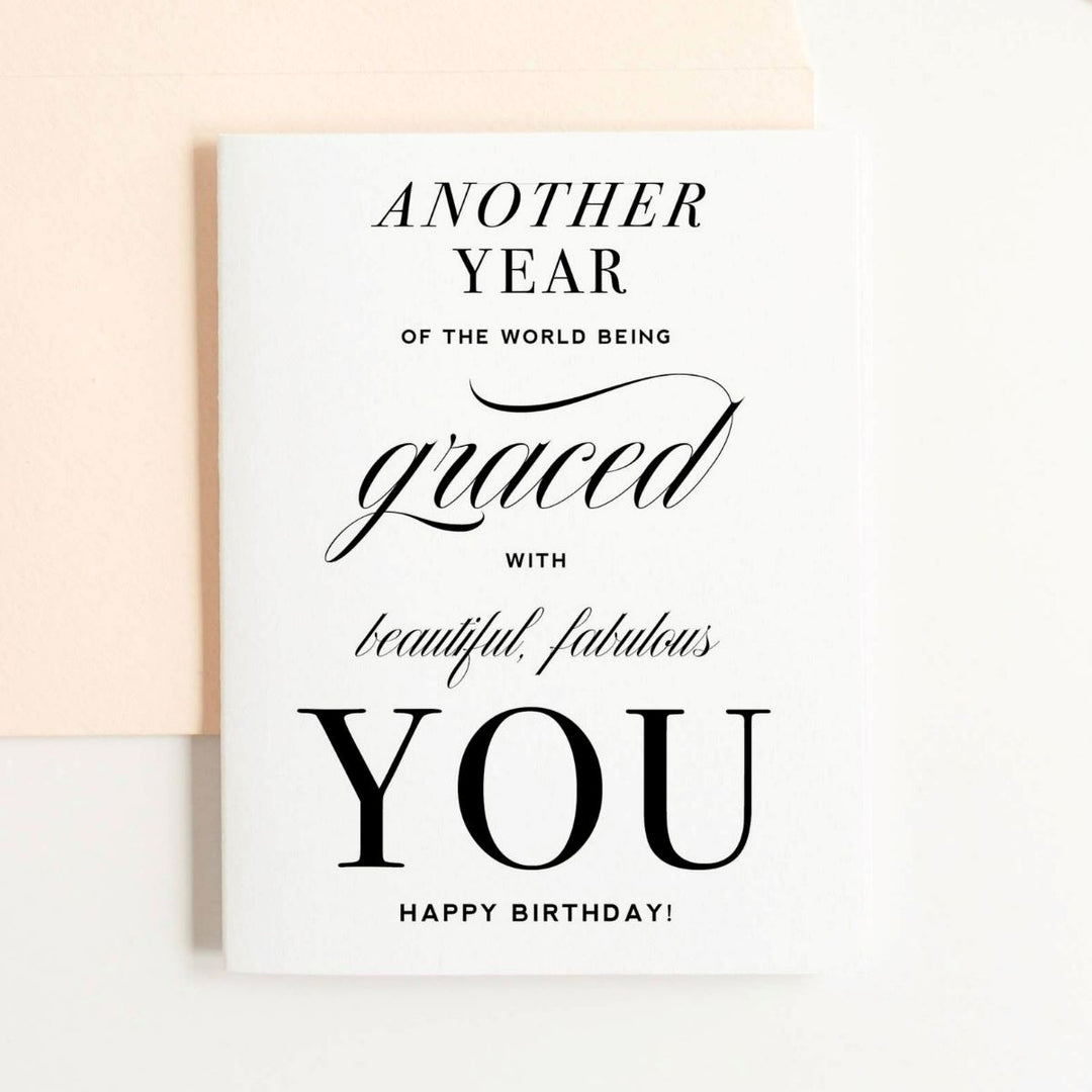 A simple white card with text that reads "Another year of the world being graced with beautiful, fabulous, you. Happy Birthday!". Comes with a cream envelope.