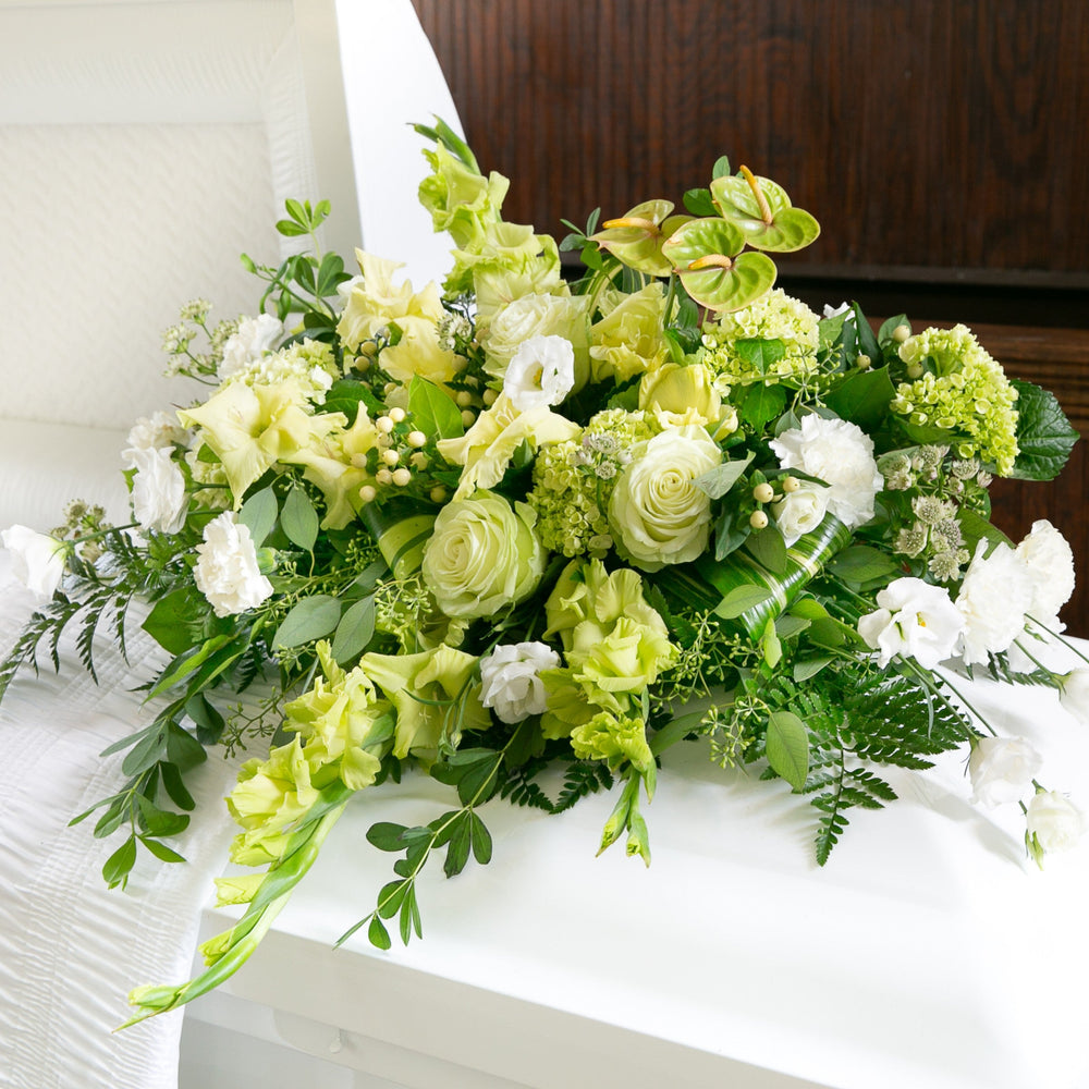Casket Bouquet of green and white flowers on a white casket with a wooden background