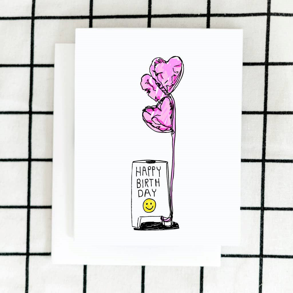 A white card with a small illustration of a foldable sign that reads "Happy Birthday" with a smiley face and pink heart shaped balloons.