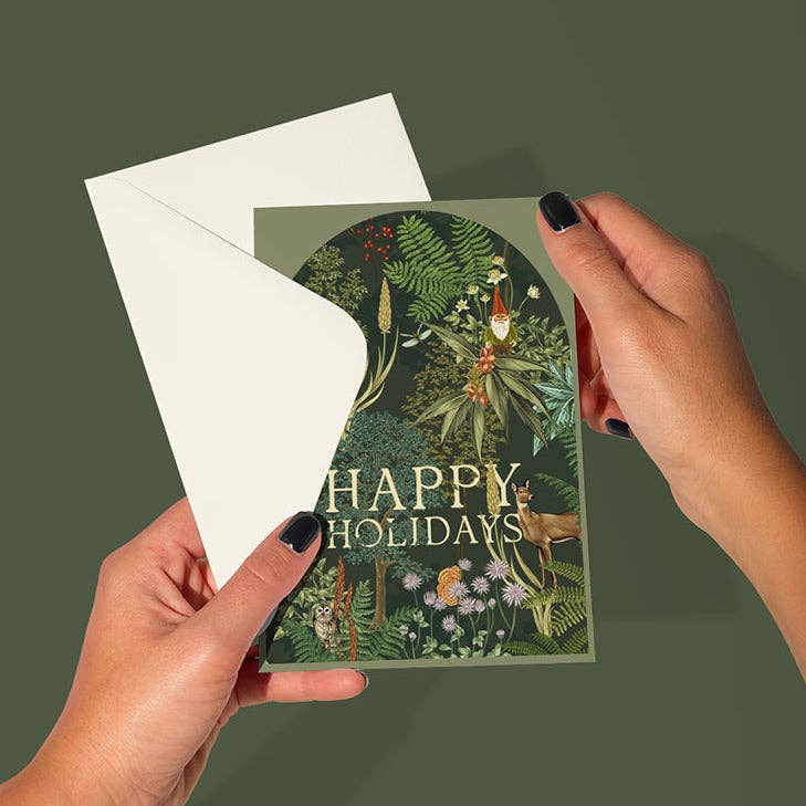 Hand holding a 'Happy Holidays' card with nature-themed design on a green background