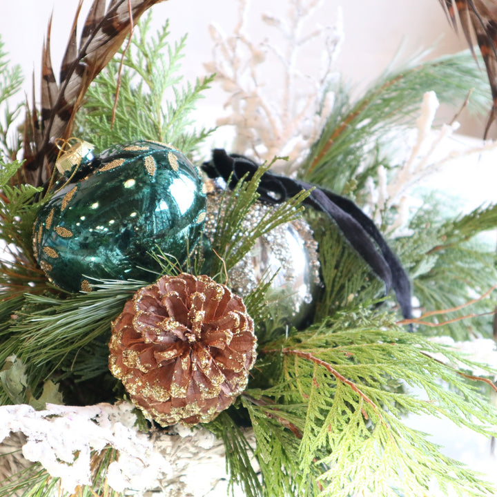 Holiday Feather | Close up on the gold tipped pinecone, tree ornaments, feather, and evergreen foliage.