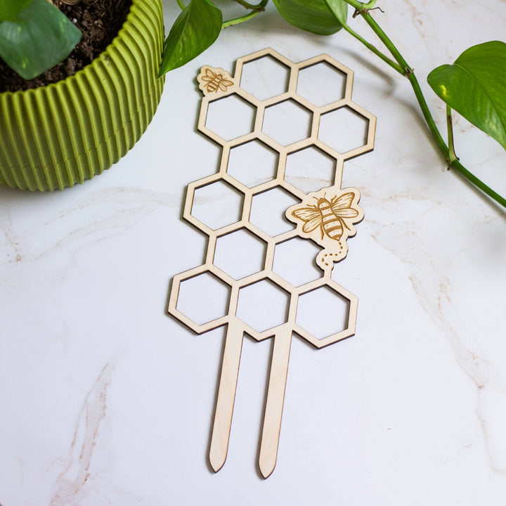 Wooden honeycomb plant support with bee decorations on a white surface.