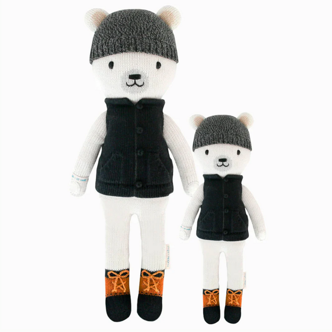 Hudson the Polar Bear | Cuddle + Kind | A white polar bear with a gray beanie, black vest and brown/black shoes. Two sizes pictured, 20" and 13".