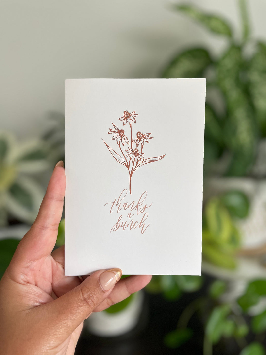 Crafted for those special moments deserving of a personal touch, this card serves as a beautiful canvas to express gratitude, love, or simply brighten someone's day with its charming illustration of a bundle of wildflowers and the lettered message "Thanks a bunch".