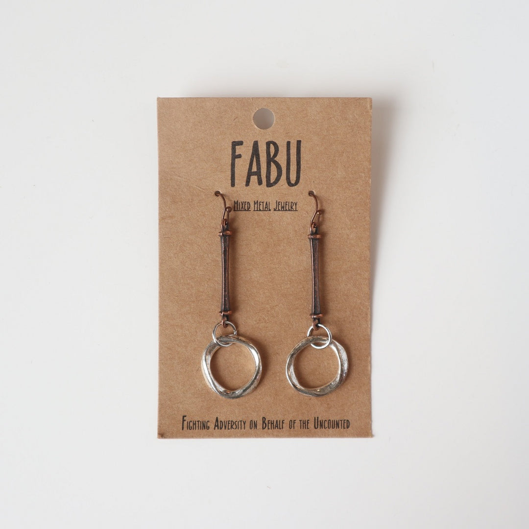 Fabu Earrings | Bronze and silver earrings that are a straight dangling piece with circle loops in silver at the bottom.  On a brown paper backing. Reads "Fabu, mixed metal jewelry, Fighting Adversity on Behalf of the Uncounted".