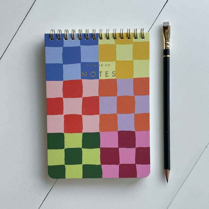 Idlewild Co. | Checked Notepad | Rainbow checkered squares on a spiral bound notepad. Text on front is gold and reads "Idlewild Co. NOTES".