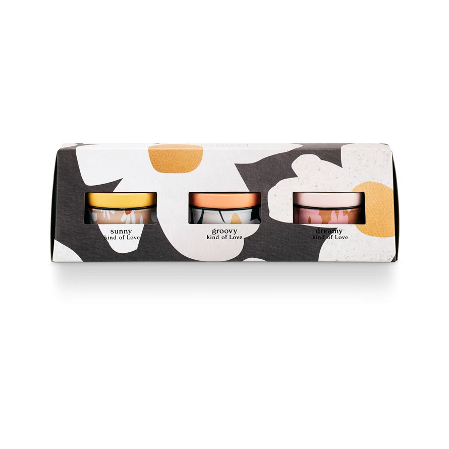 A gift set box with three different scented candles visible through the openings, featuring a love triangle design with a floral pattern in the background.