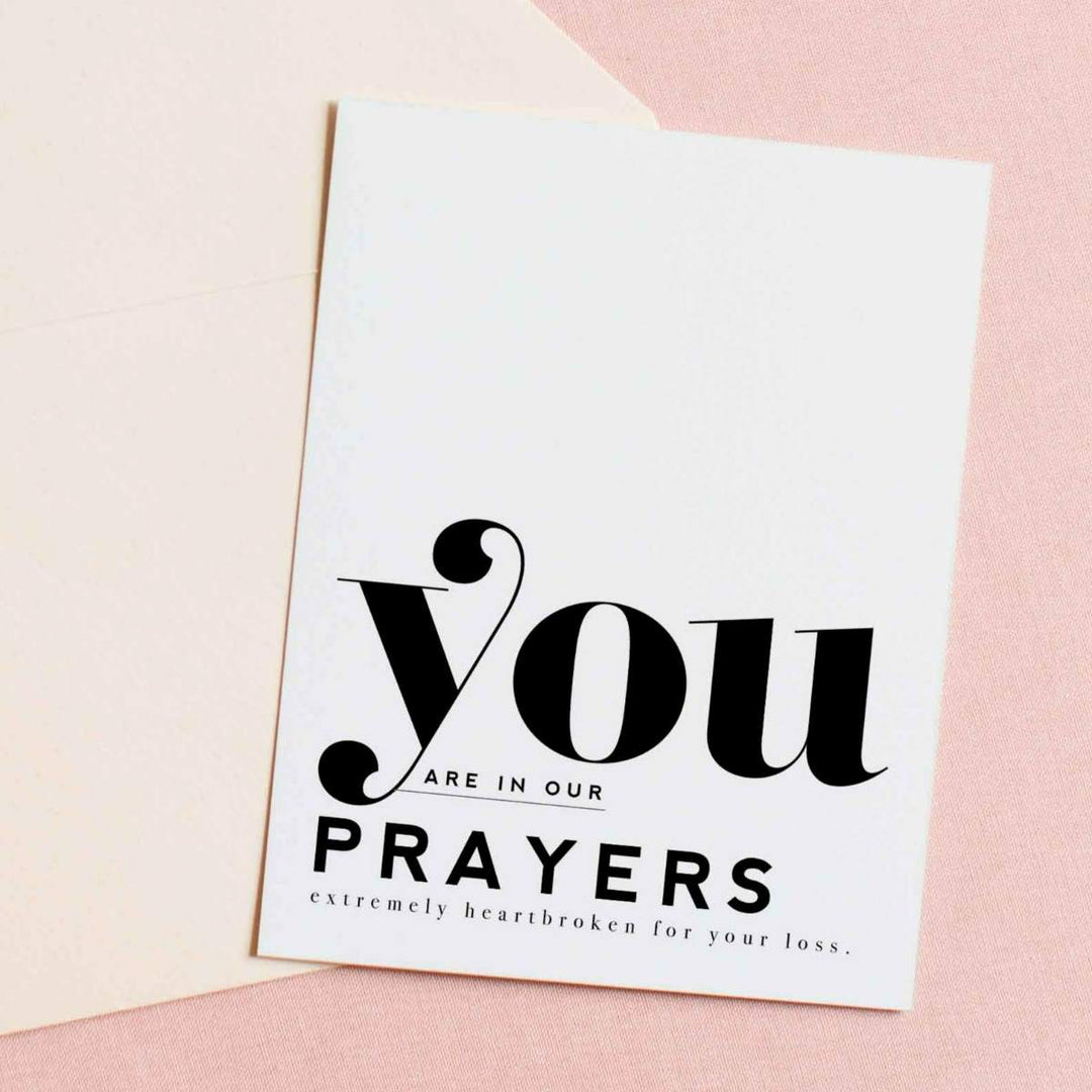 A simple white card with black text that reads "You are in our prayers. Extremely heartbroken for your loss."