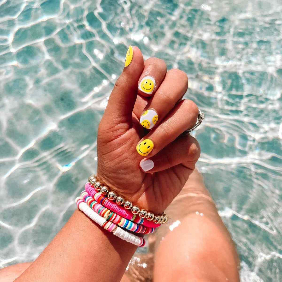 Ivy & Ash | Have A Nice Day | Yellow & White Smiley Face Nail Wrap | Model with nail wraps on in a pool.