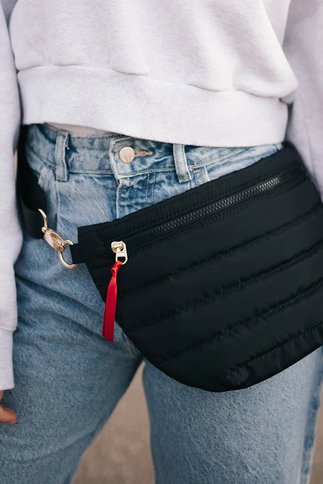 This Jolie Puffer Belt Bag in black is a trendy take on the updated fanny pack that can be worn in multiple ways. Wear it as a belt bag/fanny pack, crossbody, or shoulder bag. Features a fun half moon shape with a coordinating shiny canvas strap and gold hardware and a pop of color with ribbon accent.