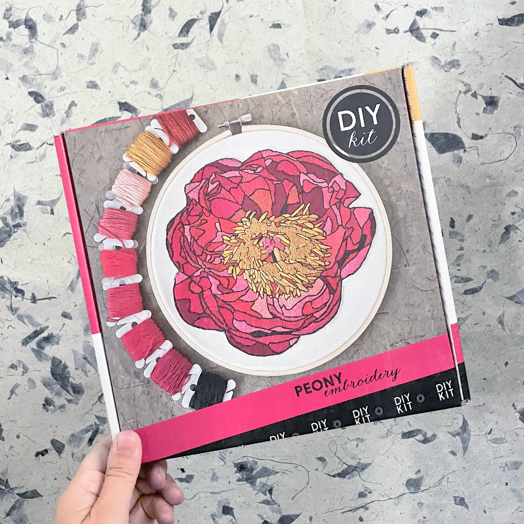 DIY embroidery kit with pink peony design on a textured surface