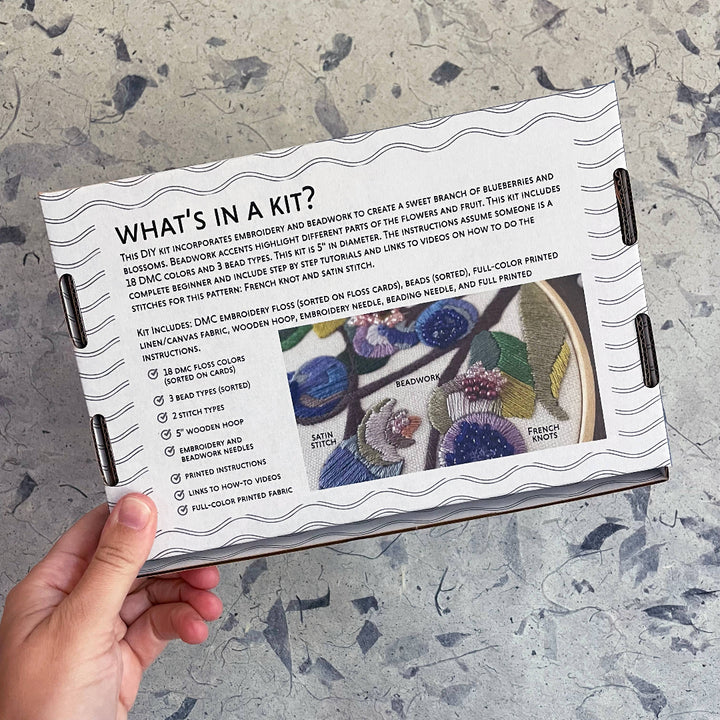 Hand holding a craft kit with embroidery design on a textured surface