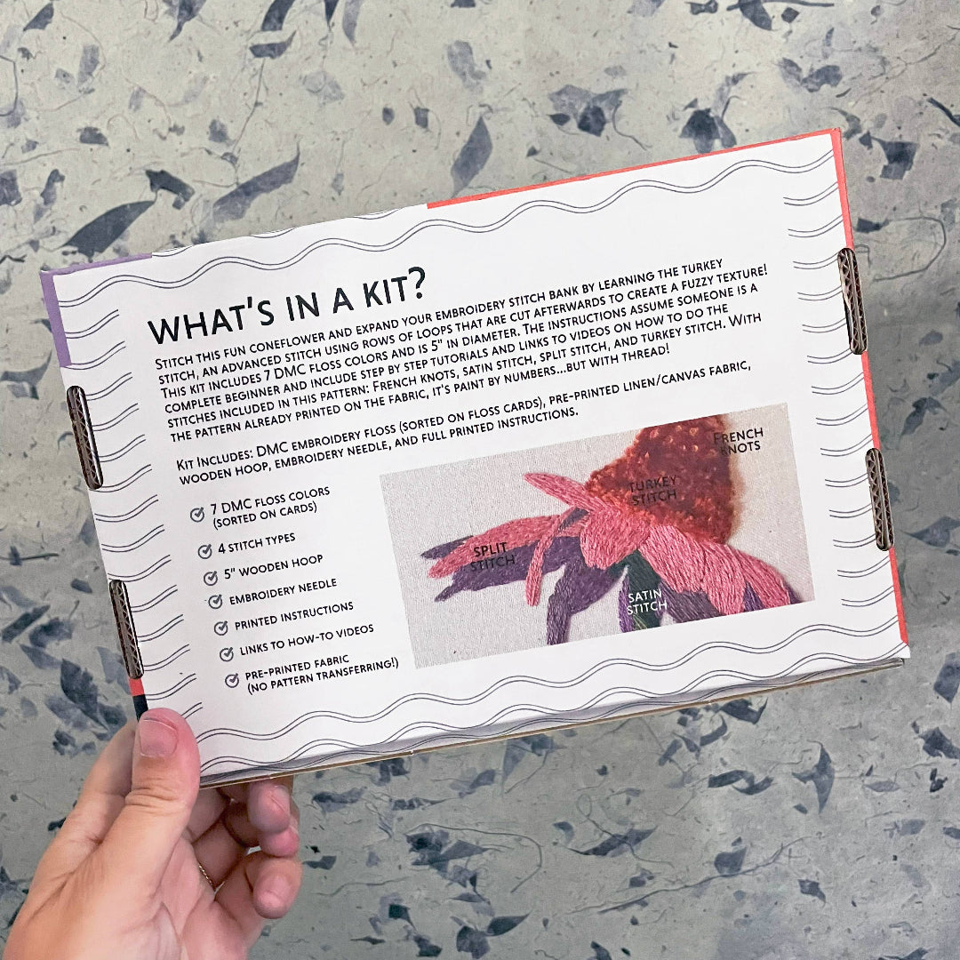 Embroidery kit information card held by a hand on a textured surface