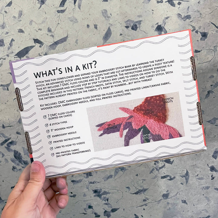 Embroidery kit information card held by a hand on a textured surface