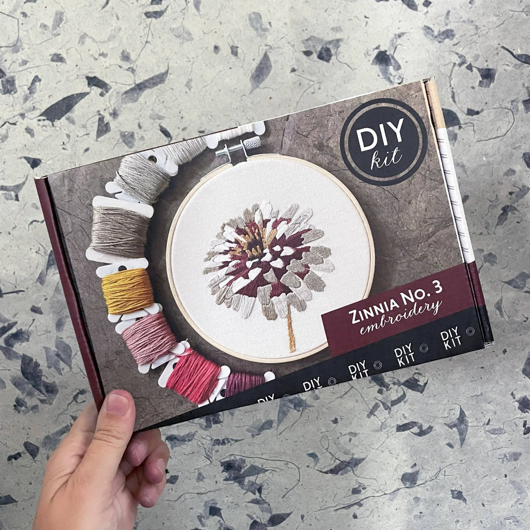 Embroidery kit packaging with yarn colors and 'DIY kit' branding on a textured surface.