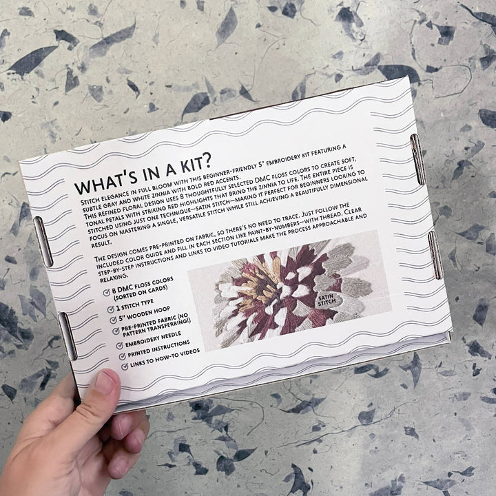 Embroidery kit packaging with text and floral design on a textured surface