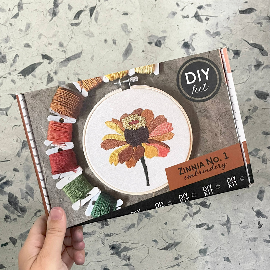 DIY embroidery kit packaging with a hand holding it on a textured surface