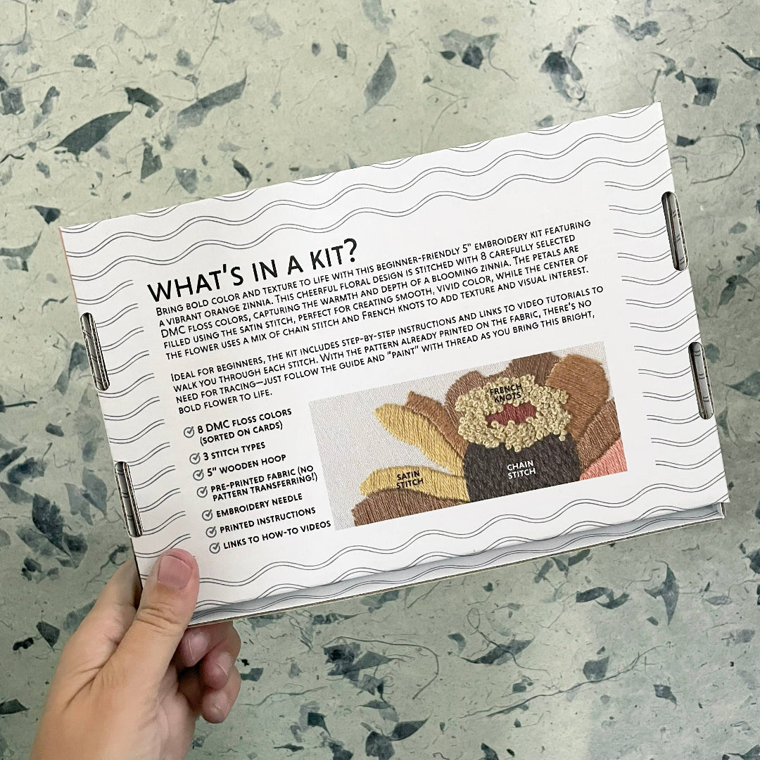 Embroidery kit packaging held by a hand on a textured surface