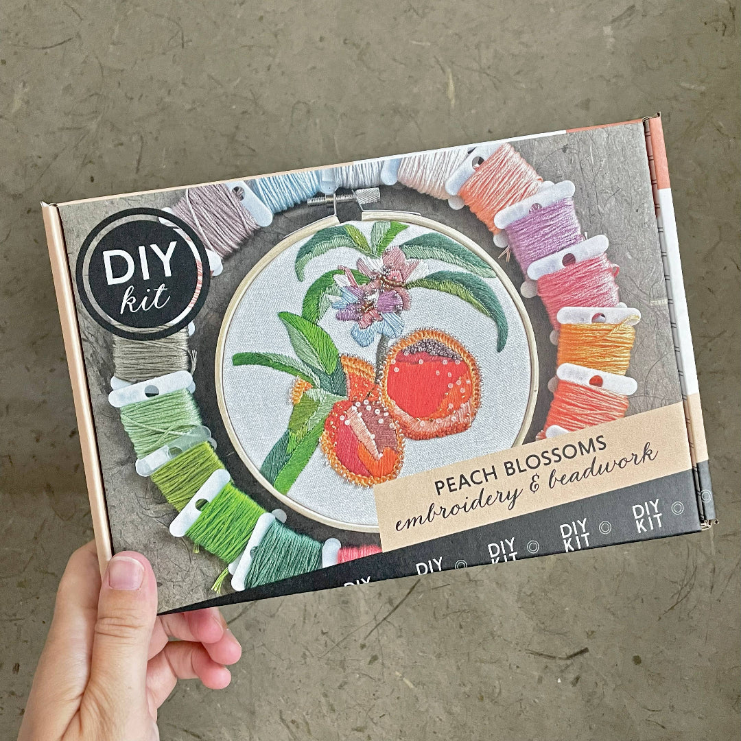 DIY embroidery kit with peach blossoms design on a cardboard box, held by a hand.