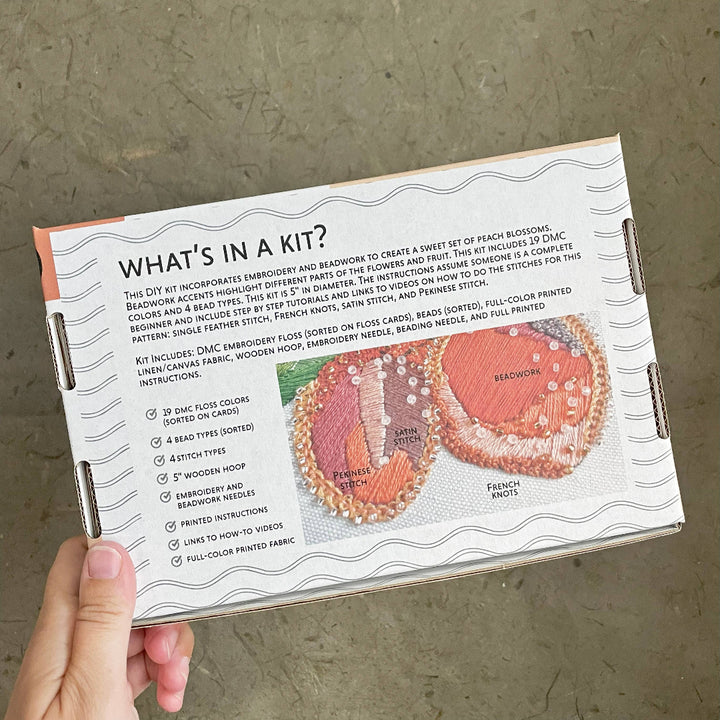 Hand holding a box with beadwork instructions and images on a concrete surface