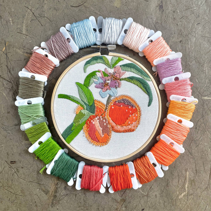 Embroidery hoop with floral design surrounded by colorful threads on a textured surface