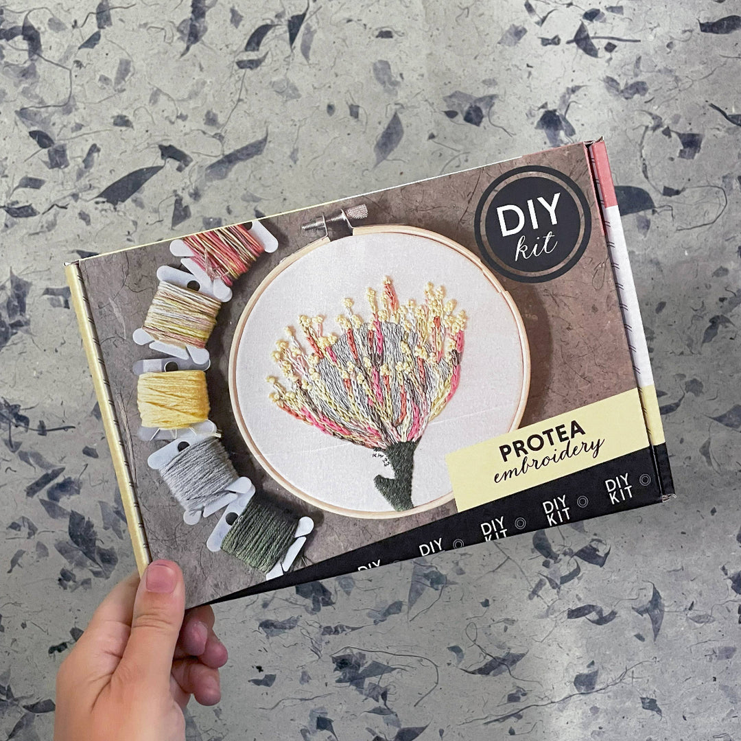 Protea embroidery DIY kit packaging held by a hand on a textured surface