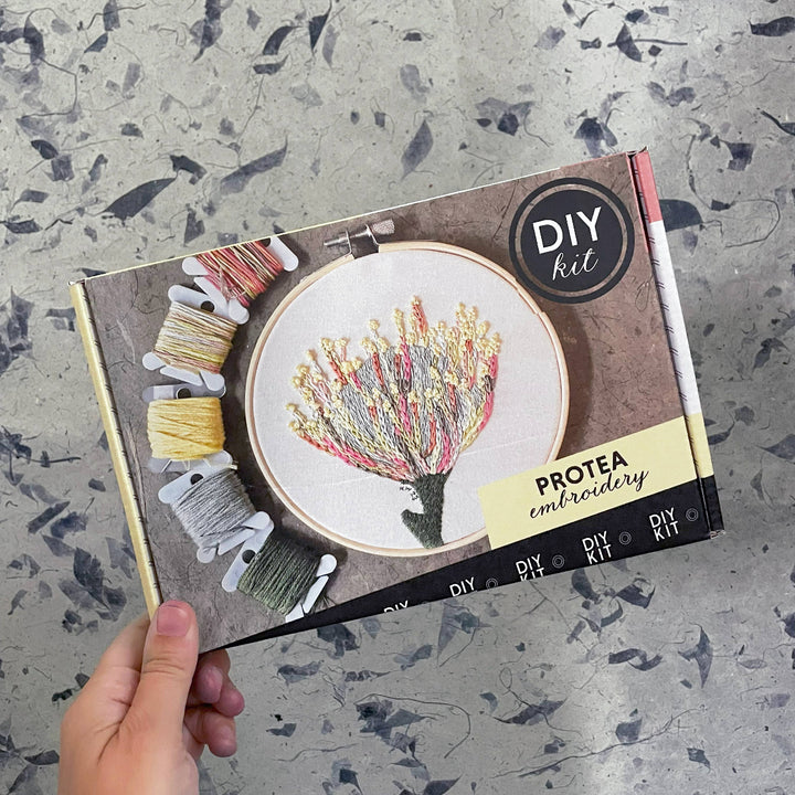 Protea embroidery DIY kit packaging held by a hand on a textured surface