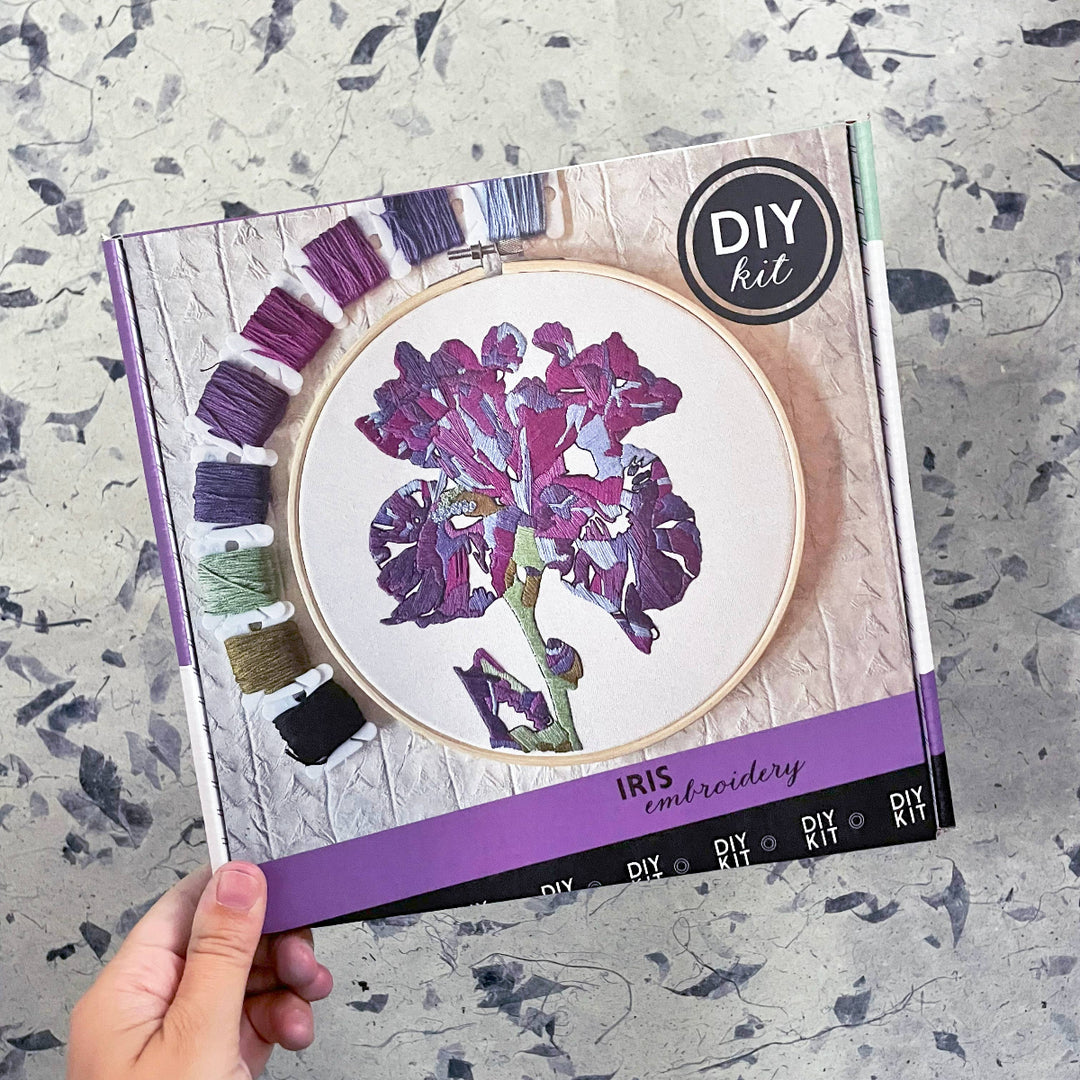 DIY iris embroidery kit packaging with a hand holding it on a textured surface