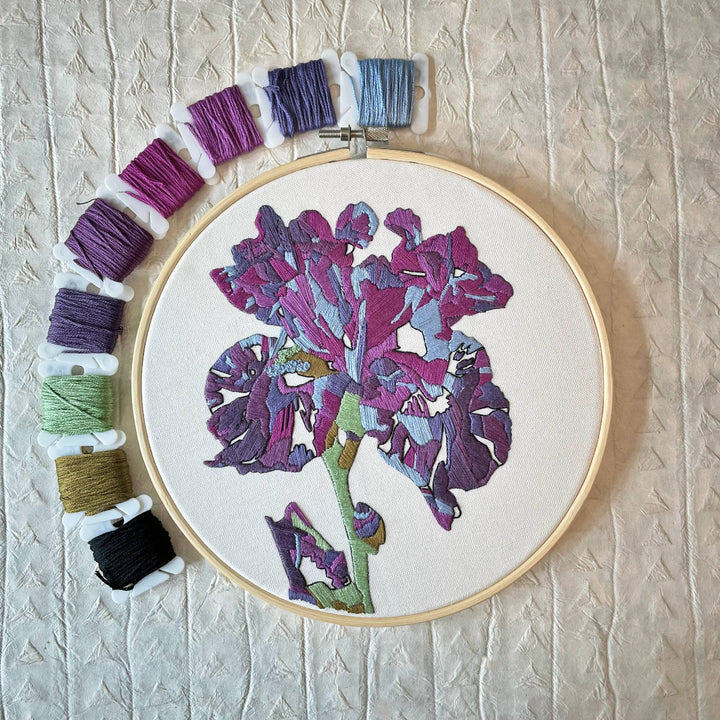 Embroidery hoop with a floral design and colorful threads on a textured beige background
