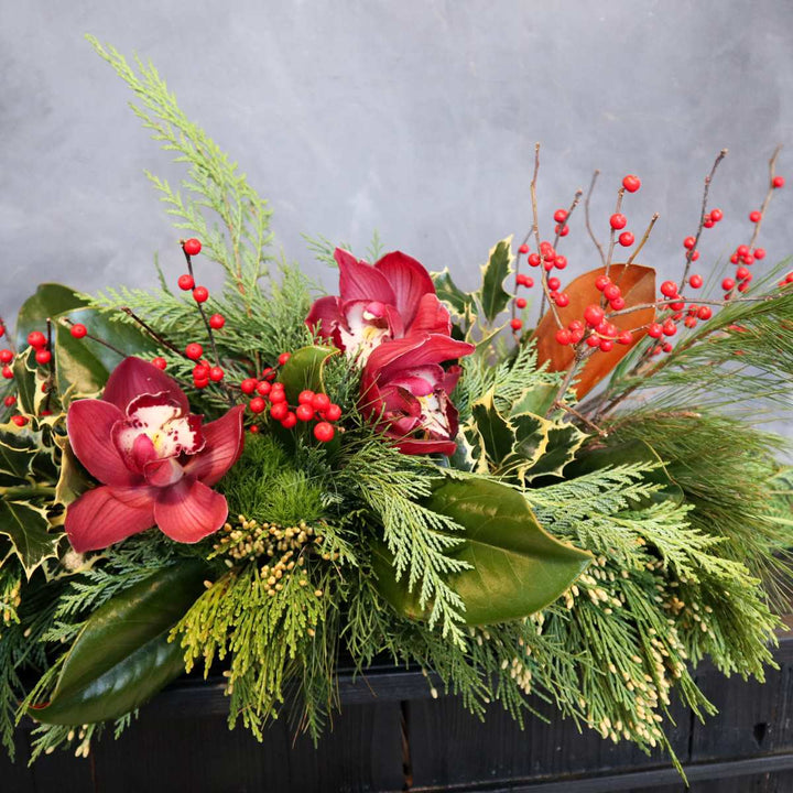 Stacy K Floral | Christmas Centerpieces, long and low with evergreens, red berries, and red orchids. Close up photo.