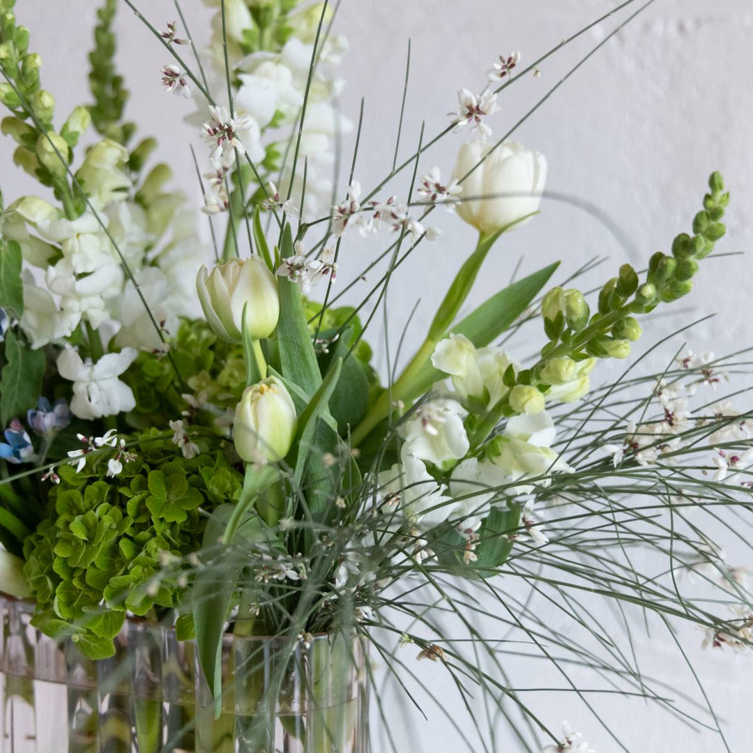 a flower arrangement with greenery and white flowers.