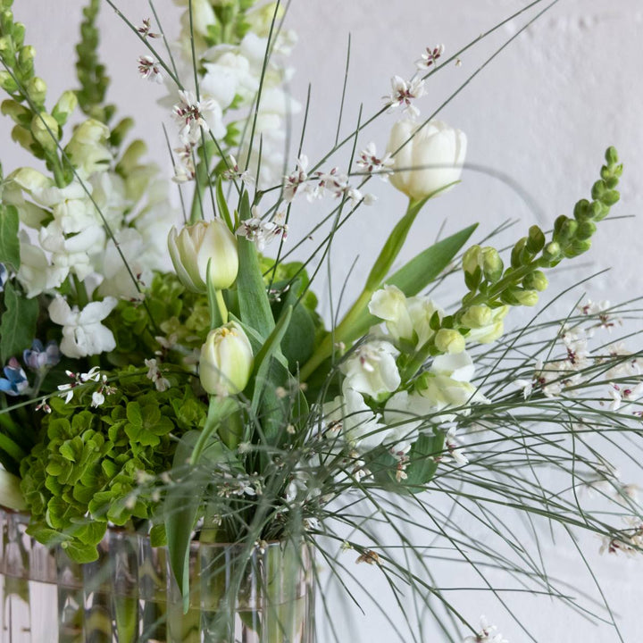 a flower arrangement with greenery and white flowers.