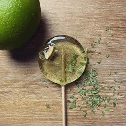 Good Lolli Lollipops | Mojito | A transparent lolli with a piece of lime and mint inside. Photo taken with a lime and dried mint in the background.