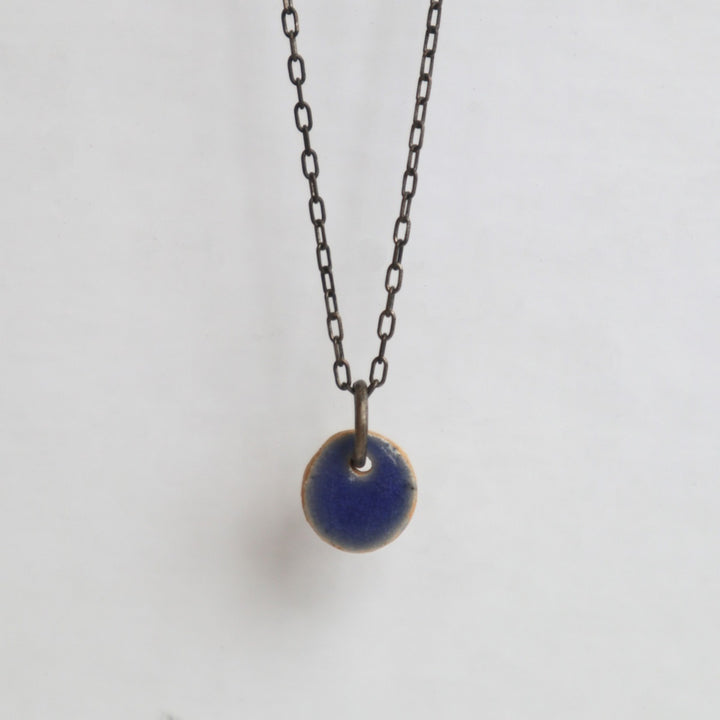 MudLOVE Necklace | A small blue circle ceramic pendant, hanging on a steel chain.