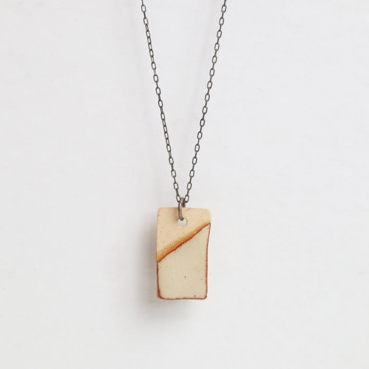 MudLOVE Necklace | A ceramic rectangle pendant on a steel chain. Glazed with white and has a red/brown edge.