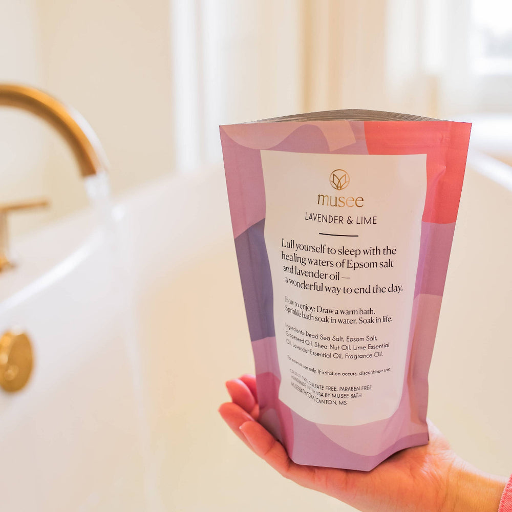 Hand holding a pink and purple product packaging in front of a sink.