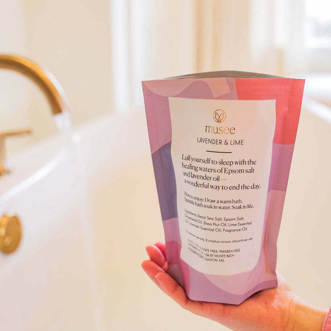 Hand holding a pink and purple product packaging in front of a sink.